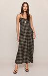 A woman modeling a black and white plaid maxi dress with spaghetti straps and a button-up front, standing against a plain light beige studio background.