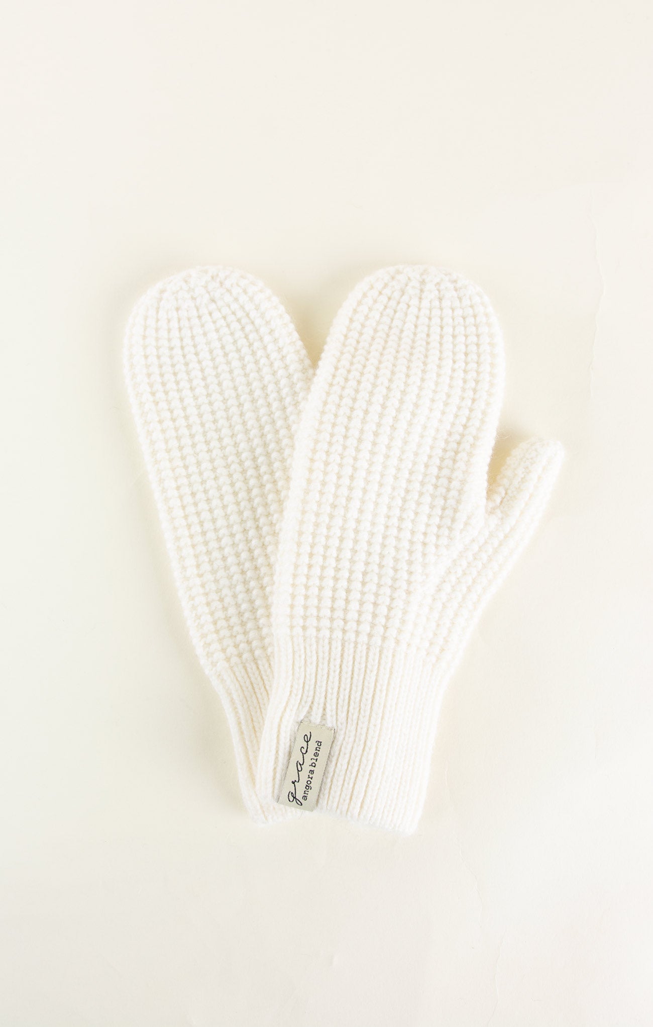 Pair of white knit mittens on a light beige background