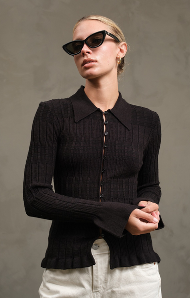Woman wearing a black ribbed sweater and sunglasses against a gray background