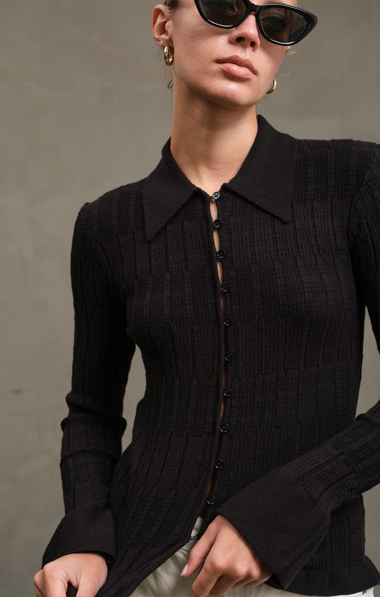 Person wearing a black ribbed sweater against a gray background