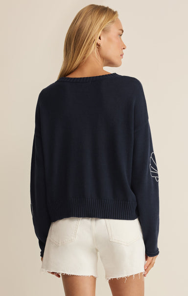 Person wearing a navy sweater with a white logo on a beige background