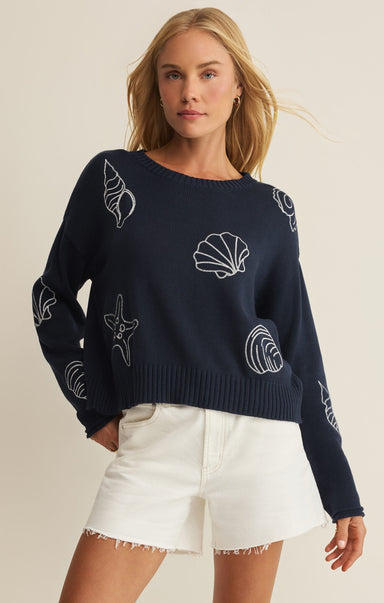Woman wearing a navy sweater with white shell patterns on a beige background