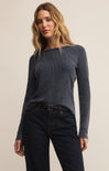 Woman wearing a blue ribbed sweater and dark jeans on a beige background