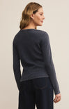Woman wearing a navy blue sweater and dark pants on a beige background