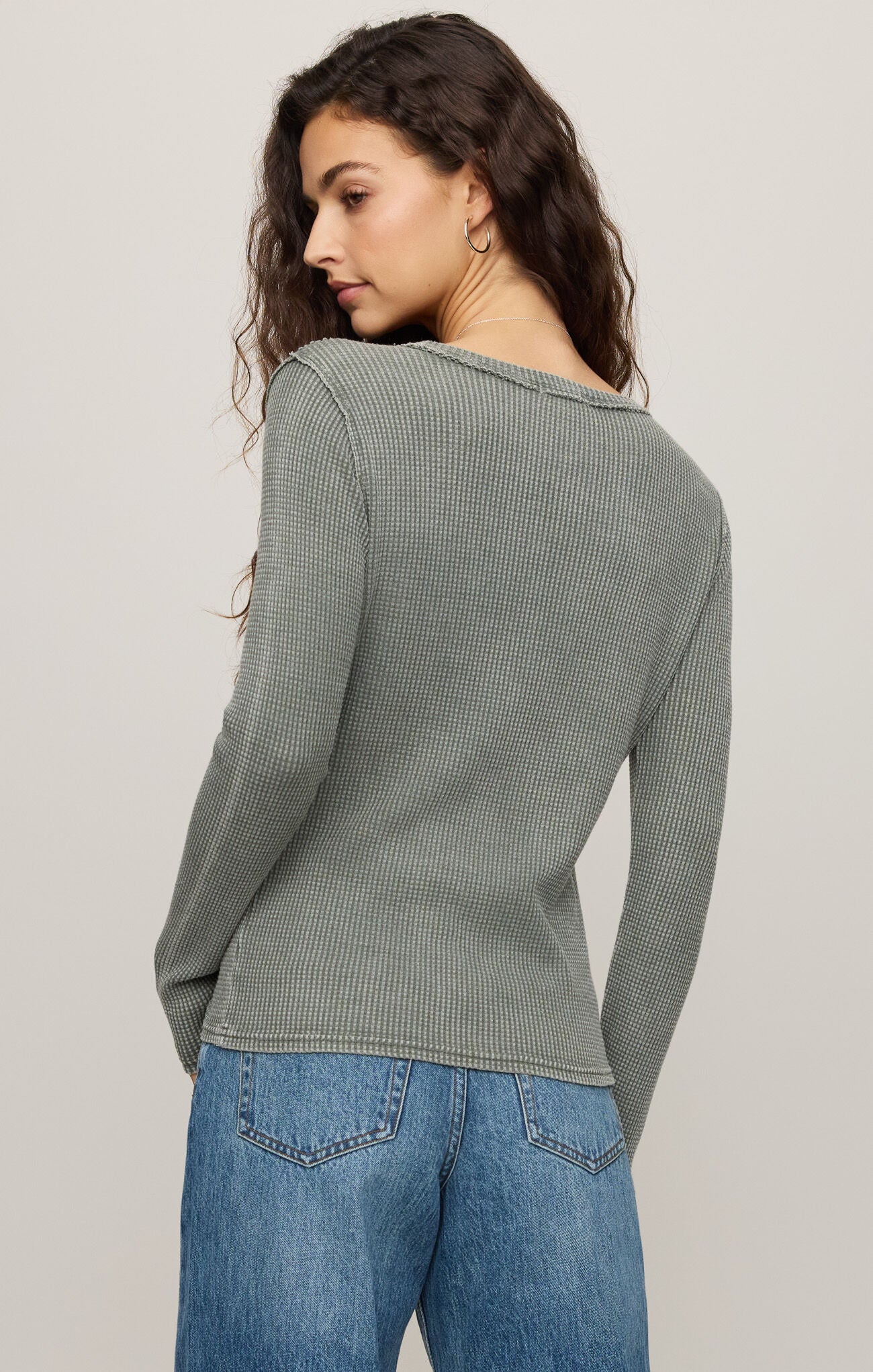 Woman wearing a green long-sleeve top and blue jeans on a plain background