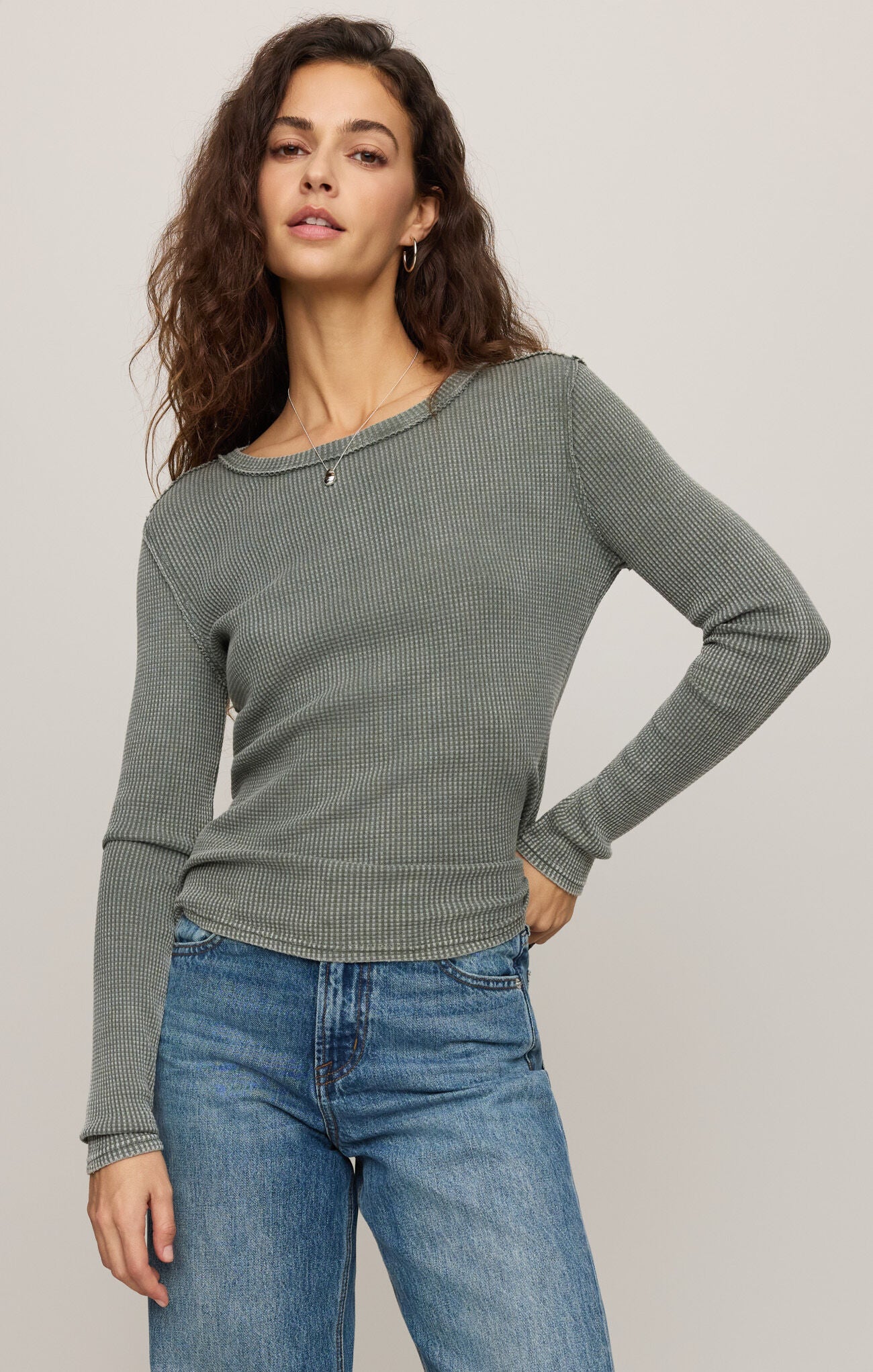 Woman wearing a green ribbed sweater and blue jeans against a plain background