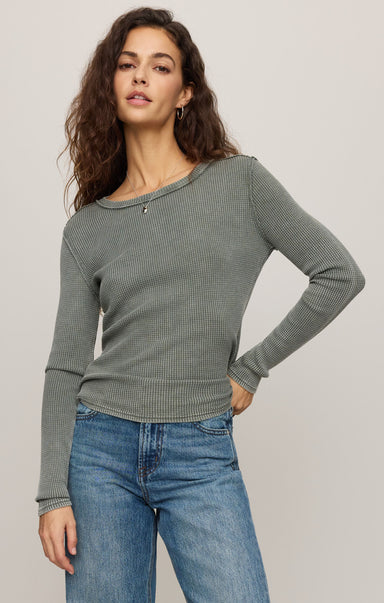 Woman wearing a green ribbed sweater and blue jeans against a plain background