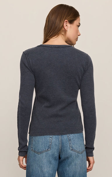 Woman wearing a dark blue textured sweater and jeans on a beige background