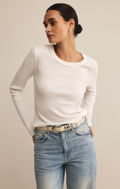 Woman wearing a white long-sleeve top and light blue jeans against a beige background
