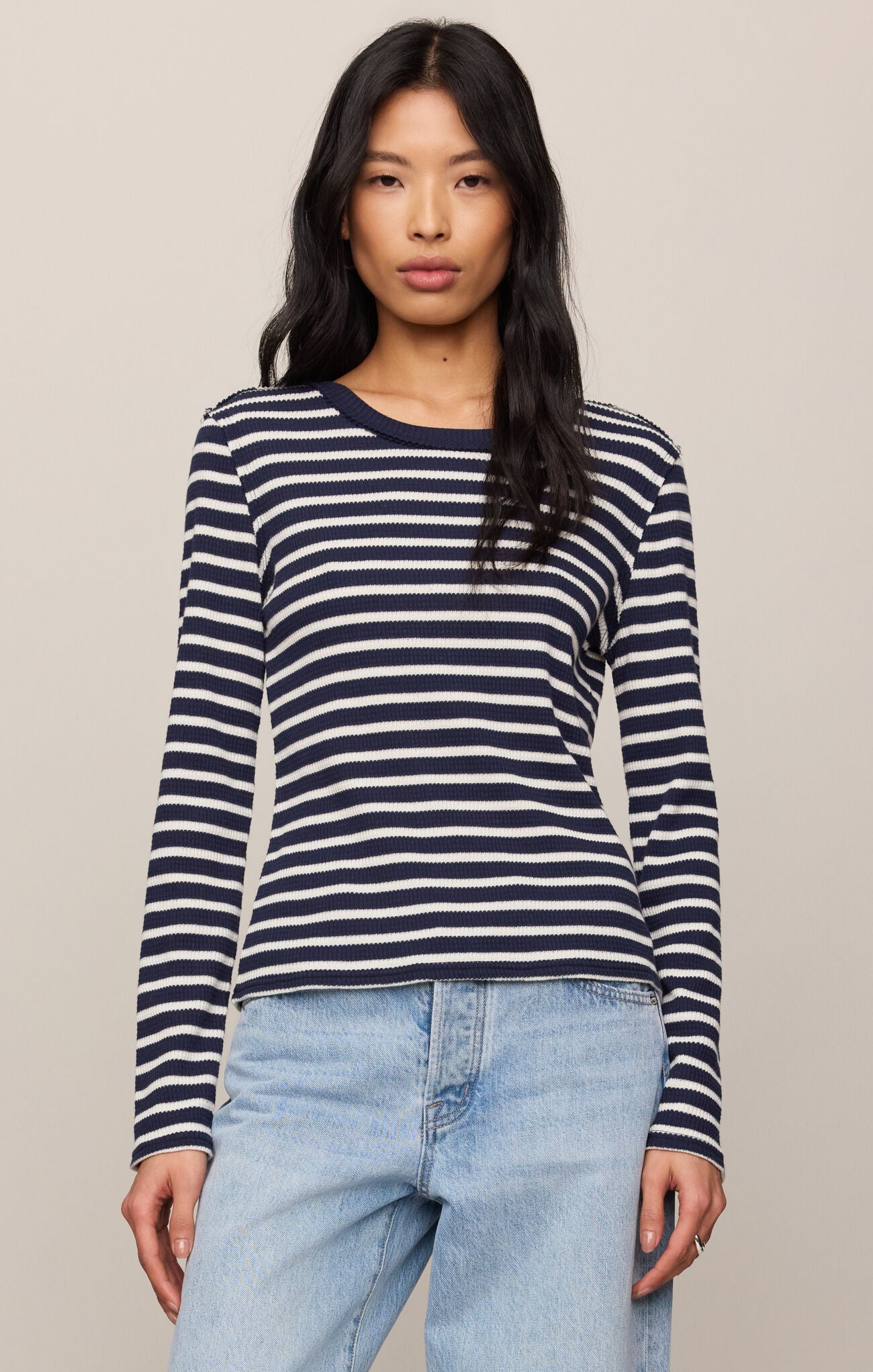 Woman wearing a navy and white striped long-sleeve shirt with light blue jeans on a beige background