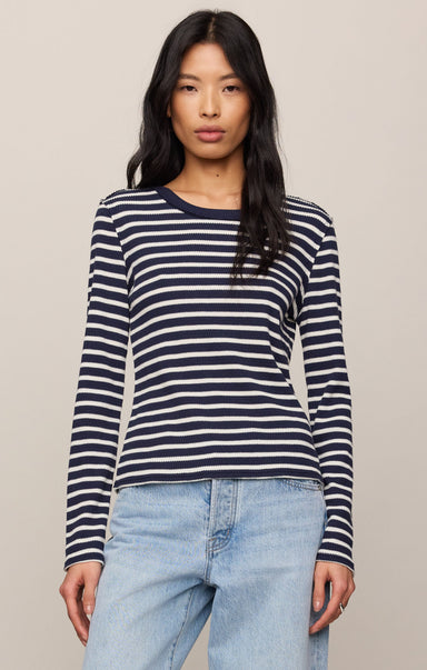 Woman wearing a navy and white striped long-sleeve shirt with light blue jeans on a beige background