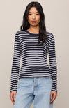 Woman wearing a navy and white striped long-sleeve shirt with light blue jeans on a beige background