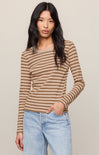 A woman modeling a long-sleeve crew-neck top with horizontal brown and beige stripes, paired with light-wash blue jeans, against a solid light beige background.