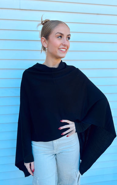 Woman wearing a black poncho against a light blue wall