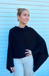 Woman wearing a black poncho against a light blue wall