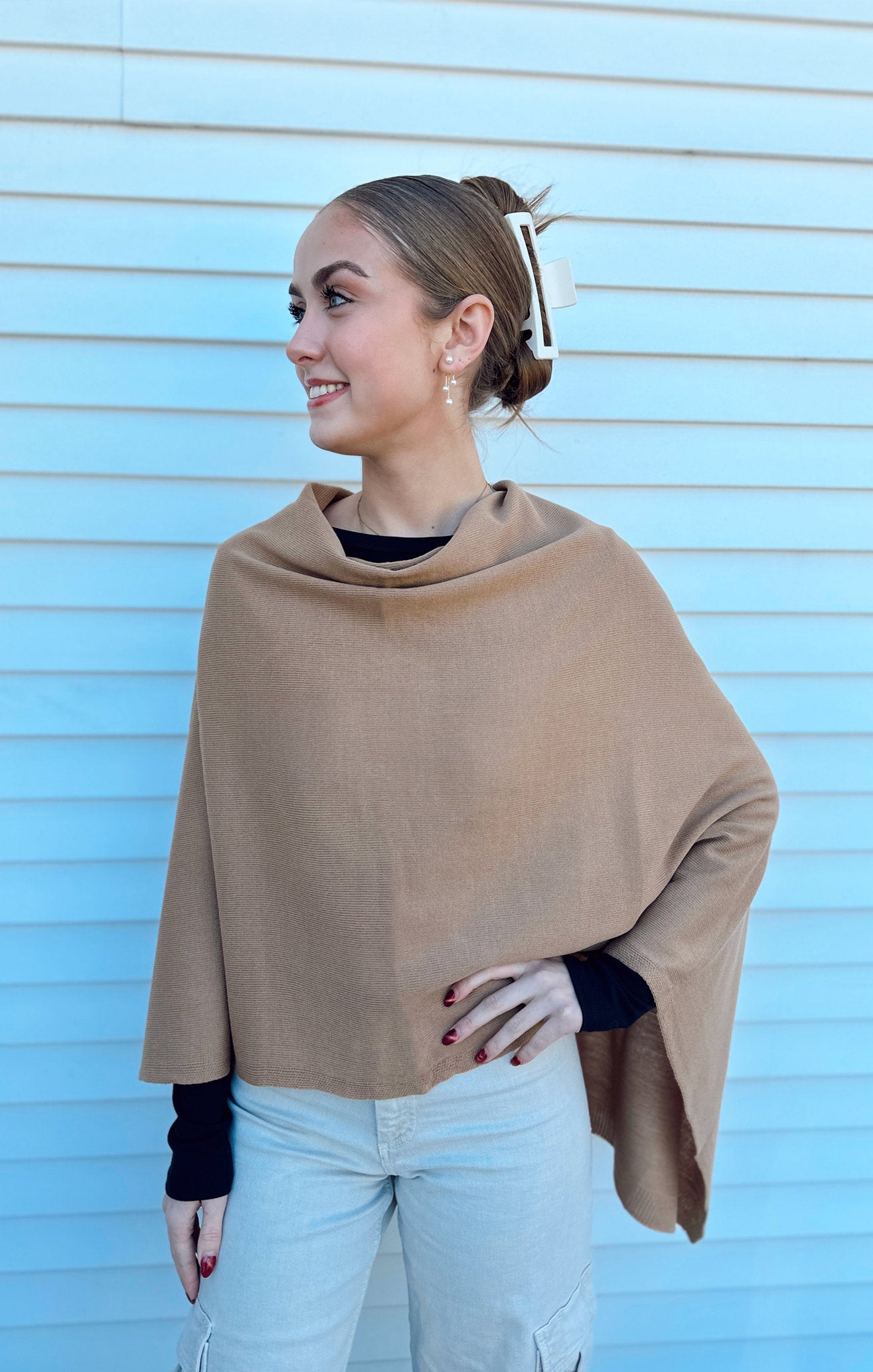 Woman wearing a beige poncho against a light blue wall