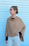 Woman wearing a beige poncho against a light blue wall