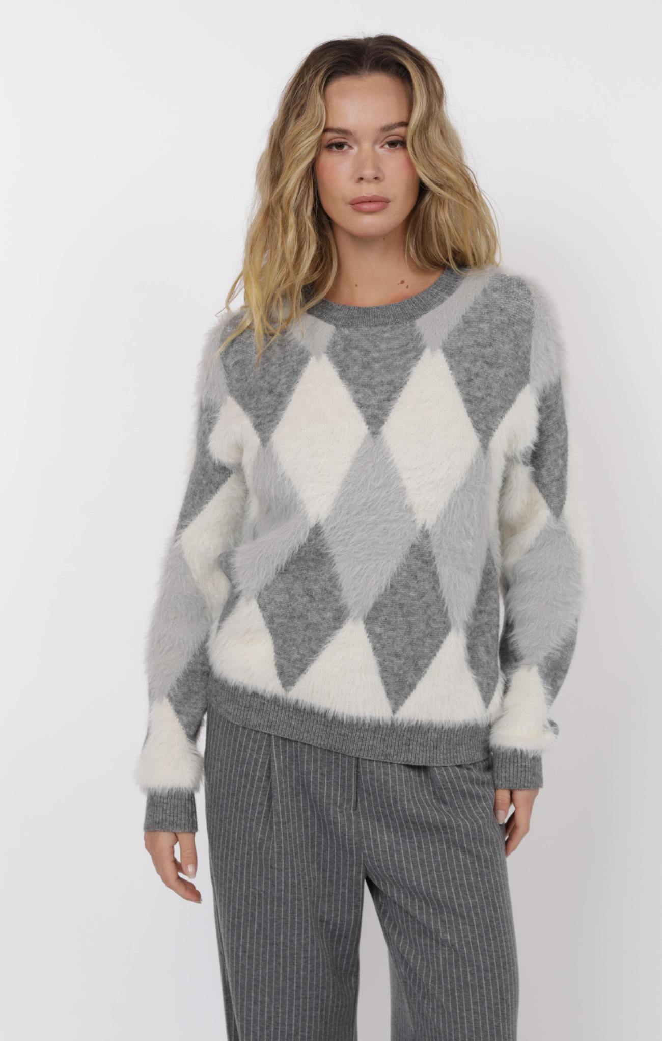 Woman wearing a gray and white argyle sweater with matching pants on a white background