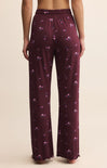 Maroon pajama pants with pink floral pattern worn by a person on a beige background