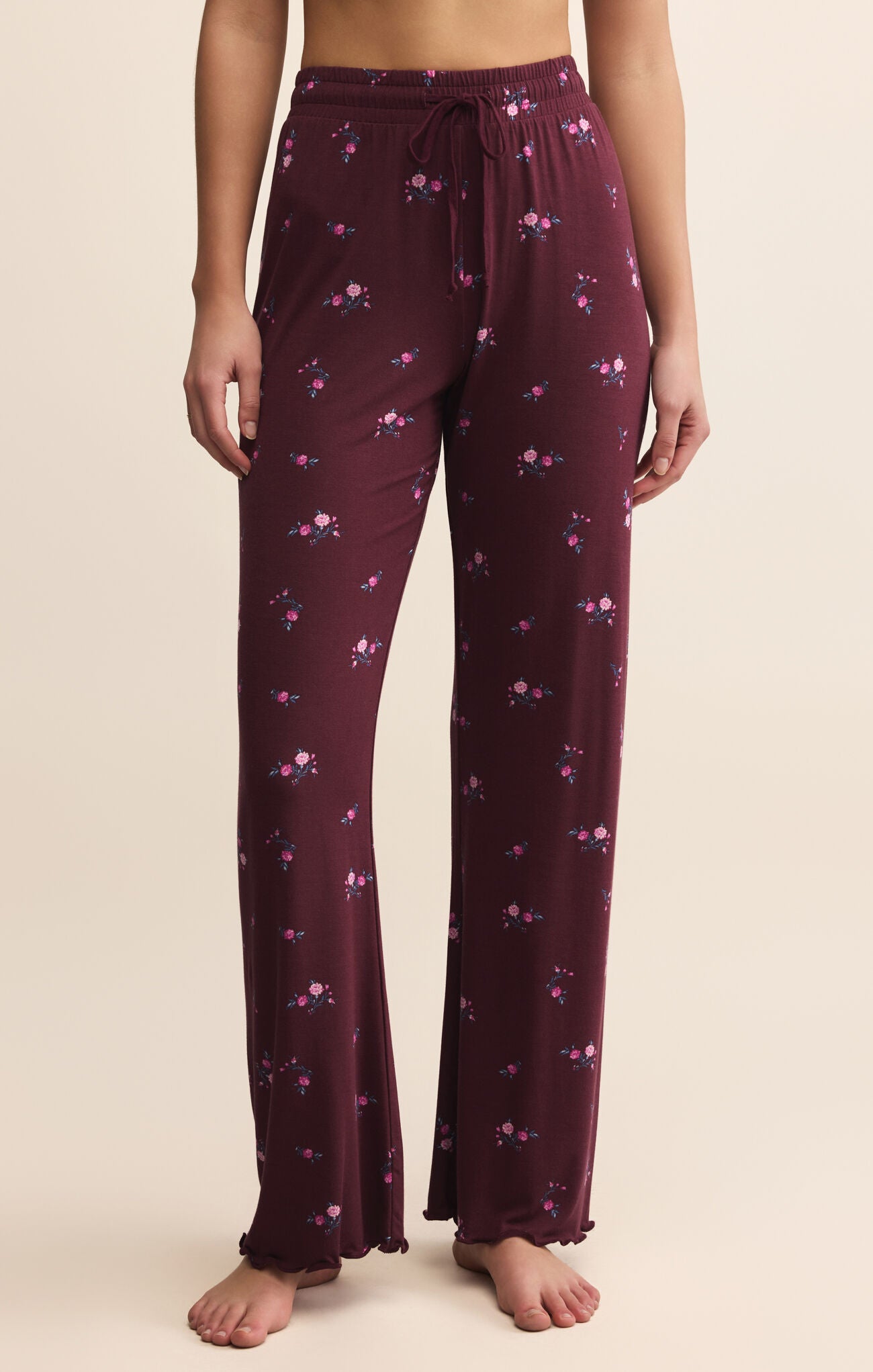 Purple pajama pants with floral pattern worn by a person on a beige background