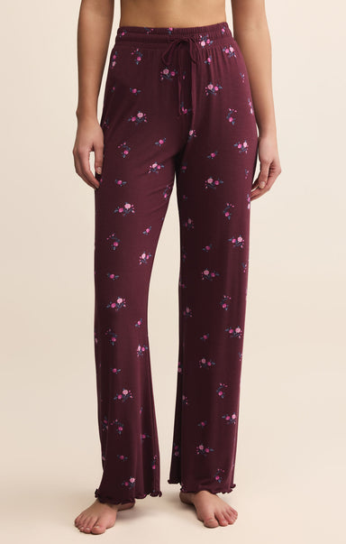 Purple pajama pants with floral pattern worn by a person on a beige background