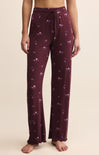 Purple pajama pants with floral pattern worn by a person on a beige background