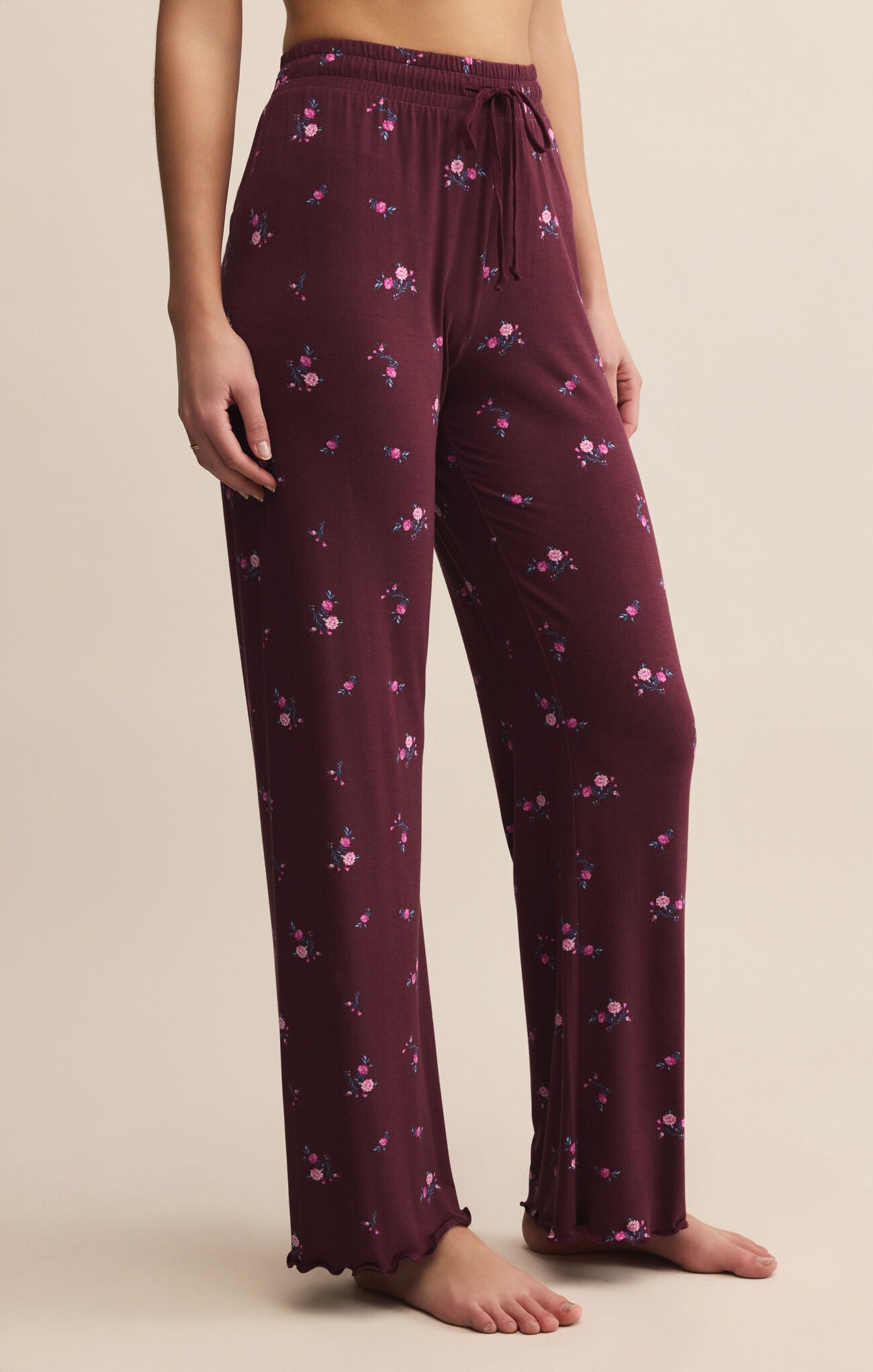 Maroon pajama pants with floral pattern worn by a person on a beige background