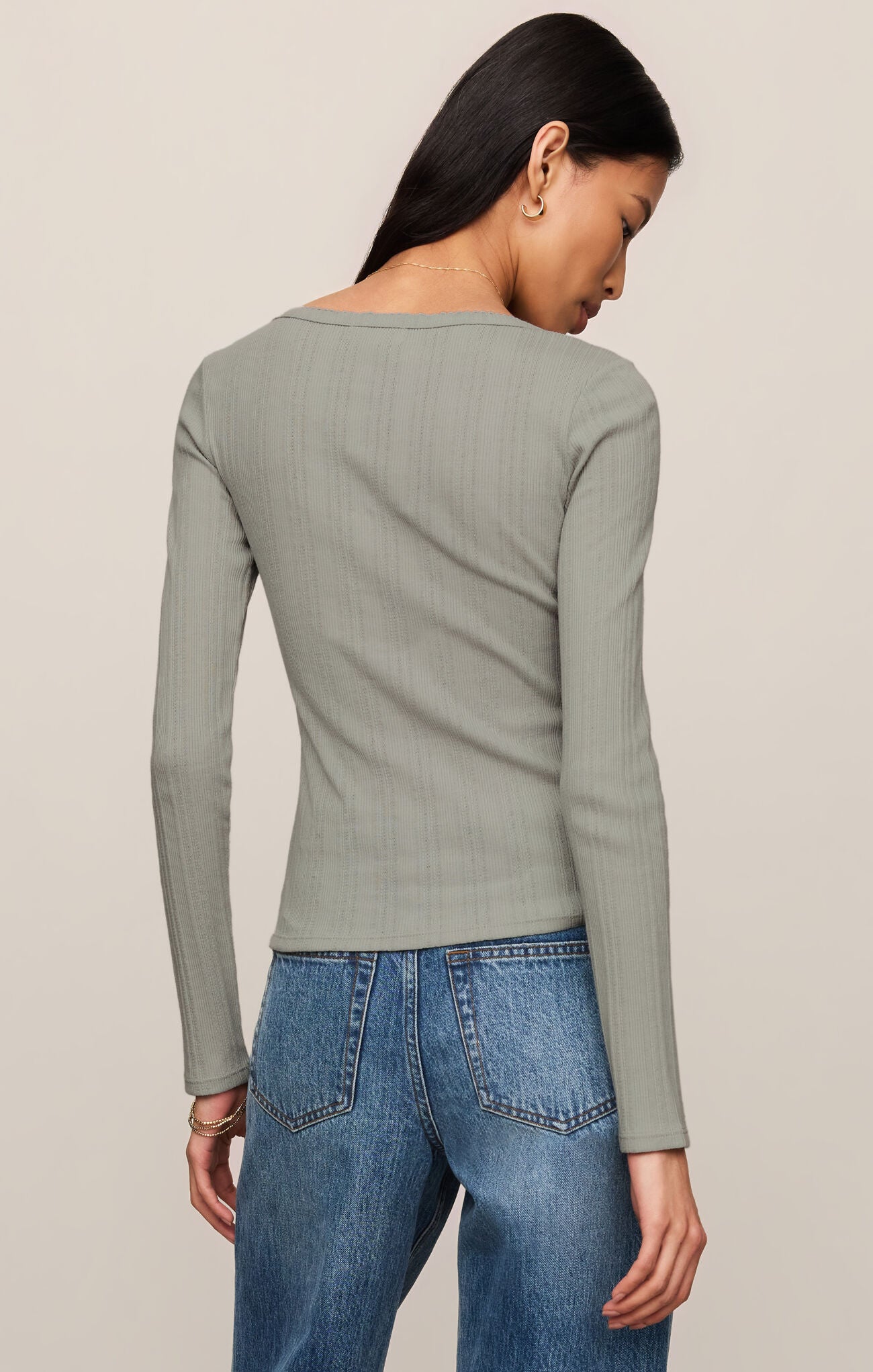 Person wearing a green ribbed long-sleeve top and blue jeans on a beige background
