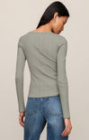 Person wearing a green ribbed long-sleeve top and blue jeans on a beige background