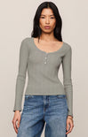 Woman wearing a green long-sleeve top and blue jeans against a beige background