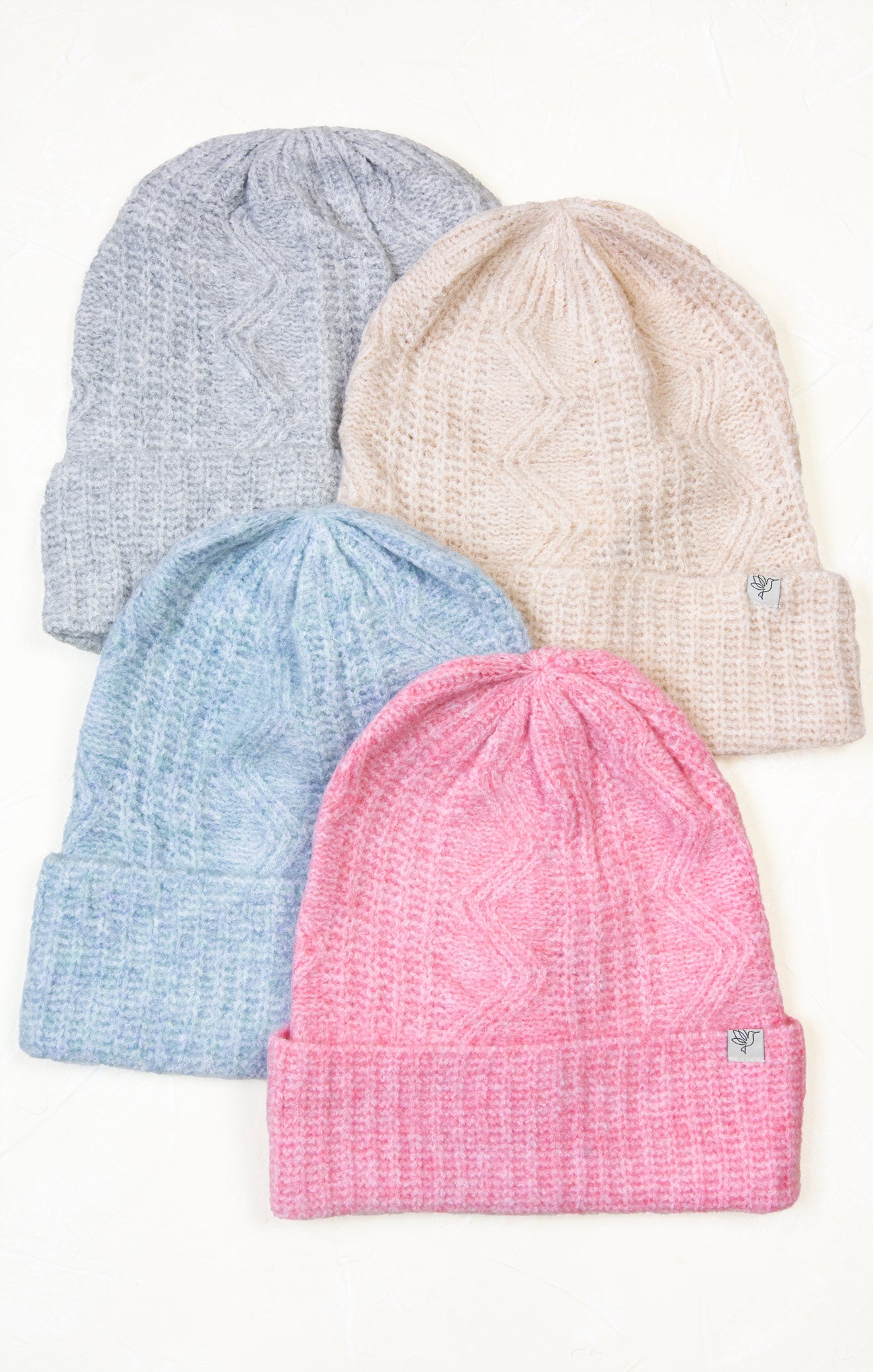 Four knit hats in pink, blue, and gray on a white background