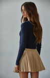 Woman wearing a navy sweater and beige pleated skirt against a plain background