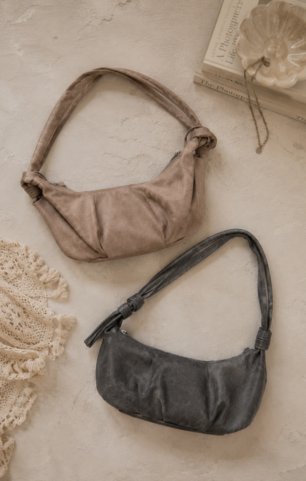 Two handbags, one brown and one black, on a textured surface with lace and books in the background.