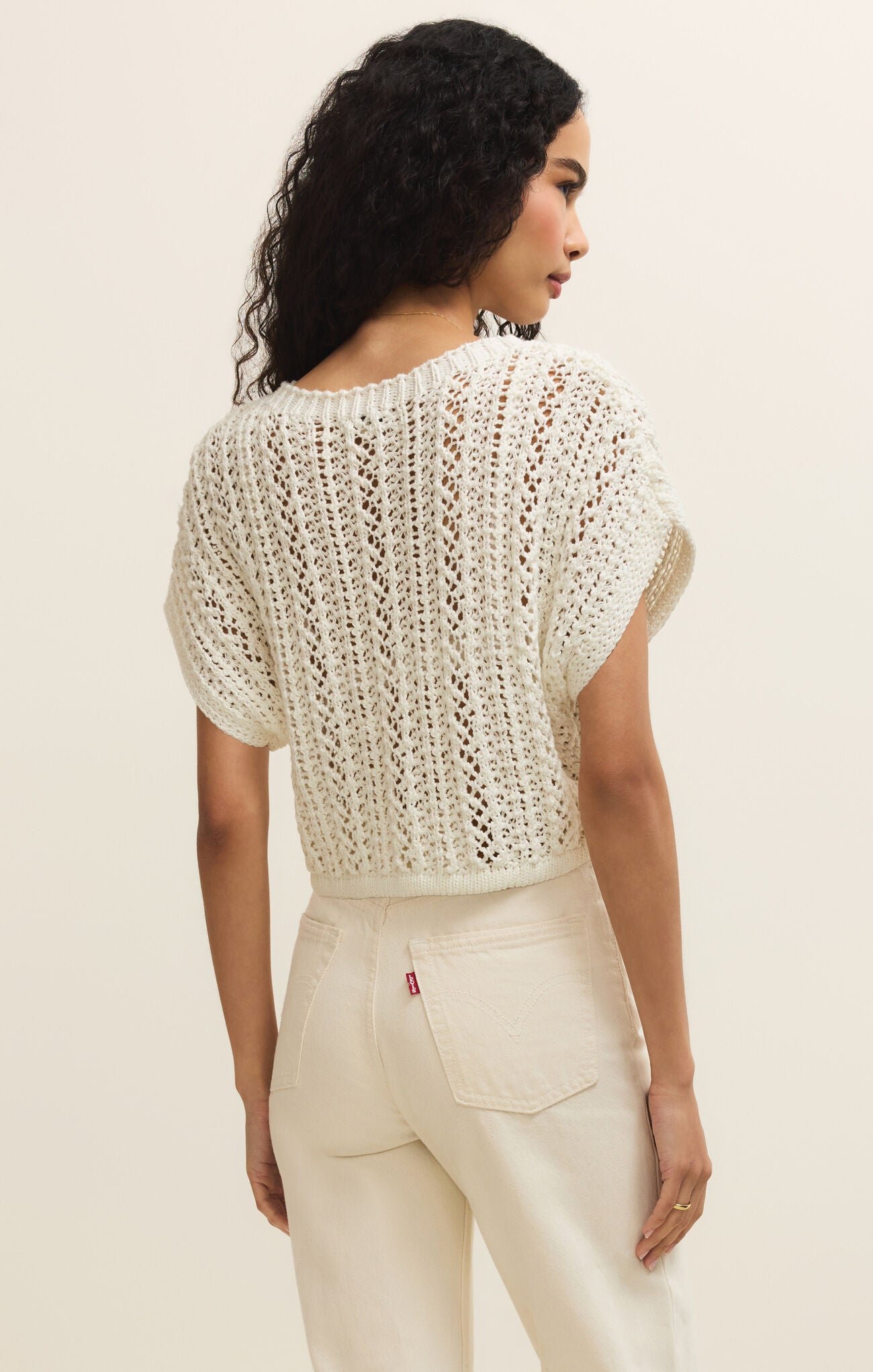 Woman wearing a white crochet top and pants against a beige background