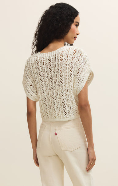 Woman wearing a white crochet top and pants against a beige background