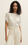 Woman wearing a white crochet top and beige pants against a plain background