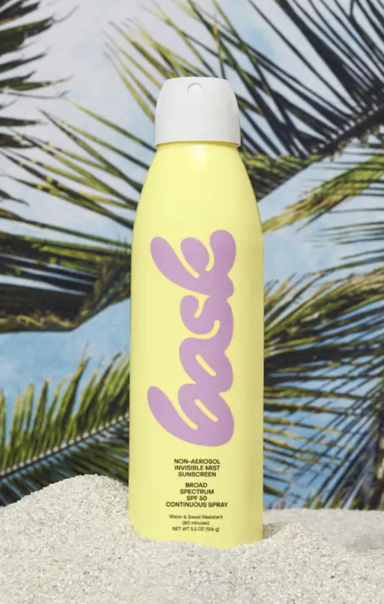 Yellow sunscreen spray bottle with purple logo against a palm leaf background