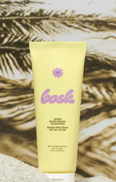 Yellow sunscreen lotion tube with 'bask' branding on a textured beige background