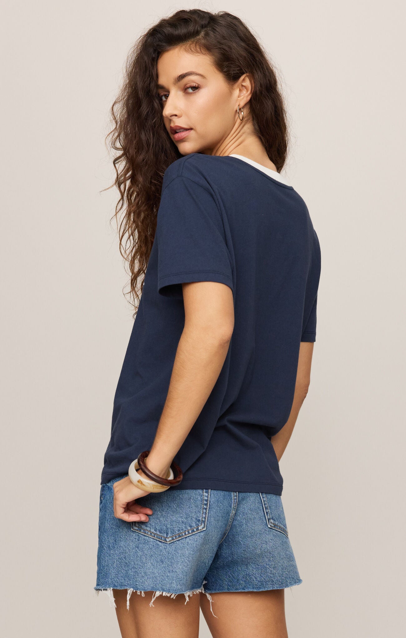 Woman wearing a navy blue t-shirt and denim shorts on a plain background