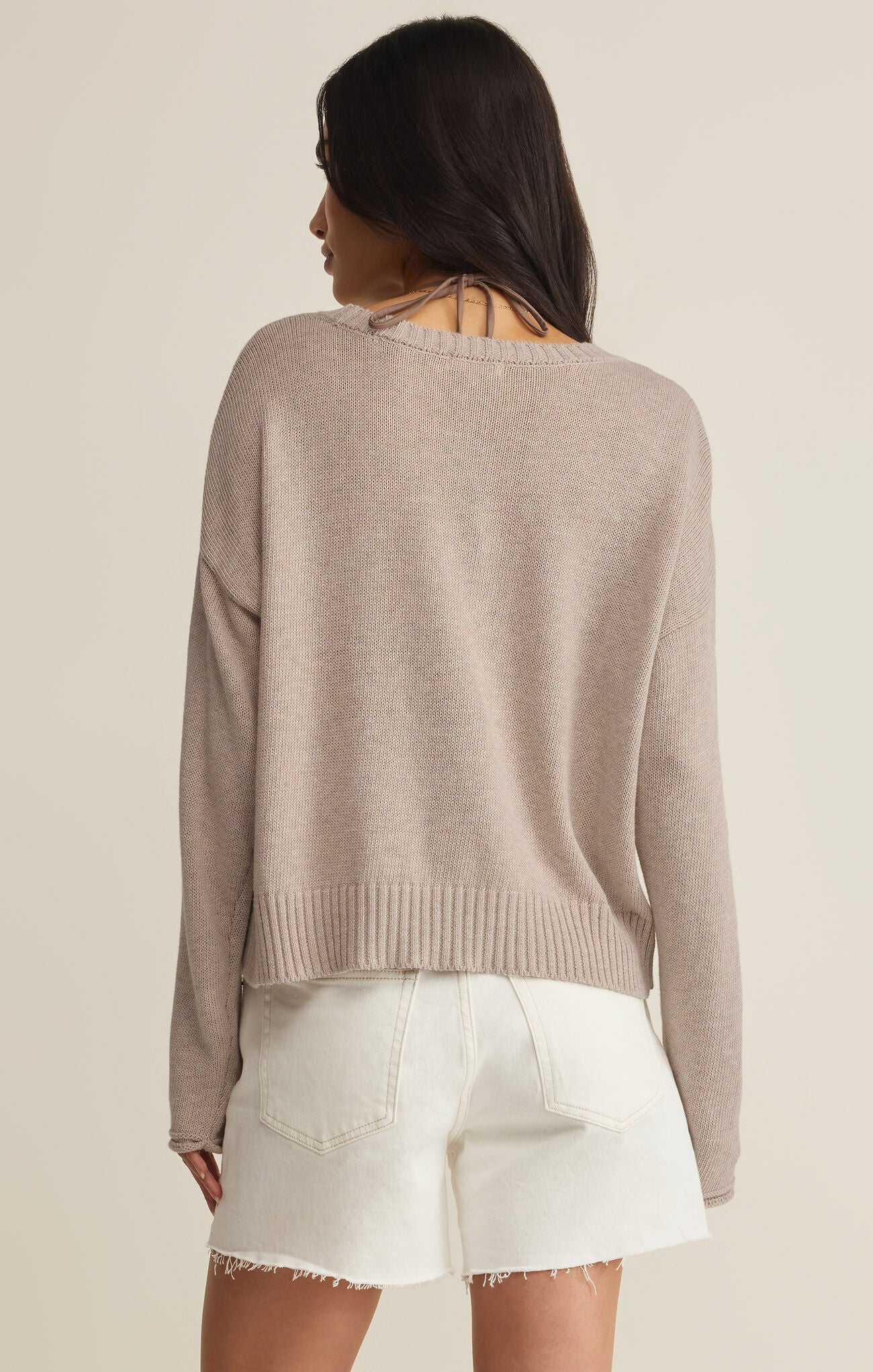 Woman wearing a beige sweater and white shorts on a plain background