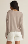 Woman wearing a beige sweater and white shorts on a plain background