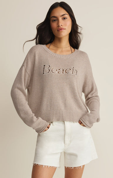 Woman wearing a gray sweater with 'Beach' text and white shorts on a beige background