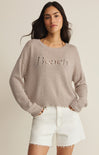 Woman wearing a gray sweater with 'Beach' text and white shorts on a beige background