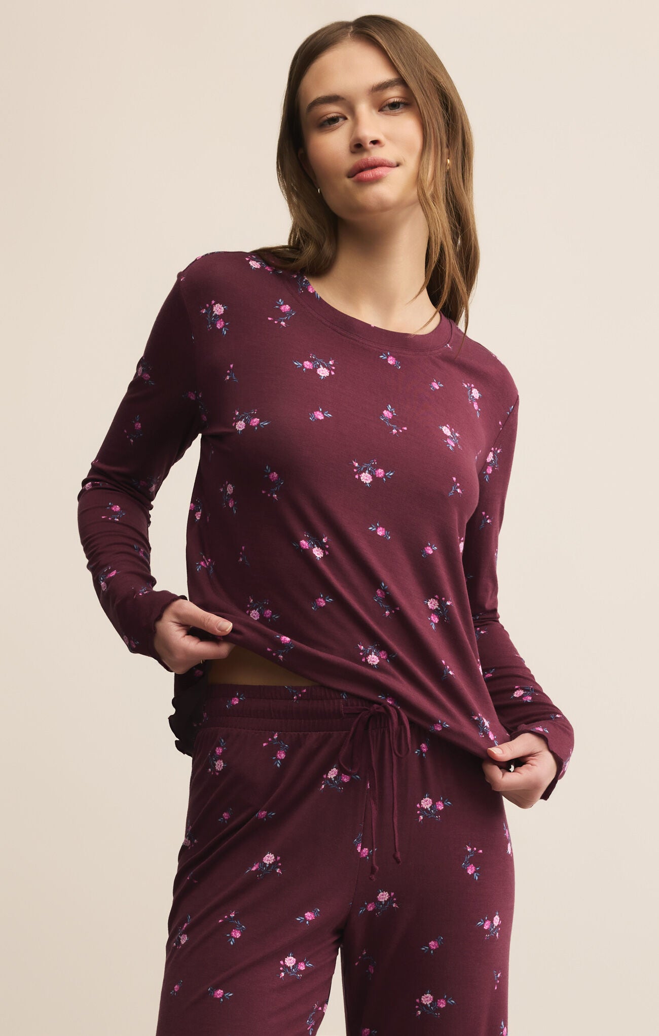 Woman wearing a maroon long-sleeve top and pants with floral patterns on a beige background