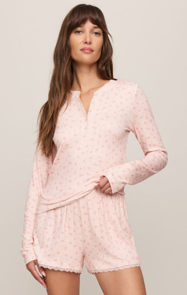 Woman wearing a pink pajama set with long sleeves and shorts on a light background
