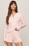 Woman wearing a pink pajama set with long sleeves and shorts on a light background
