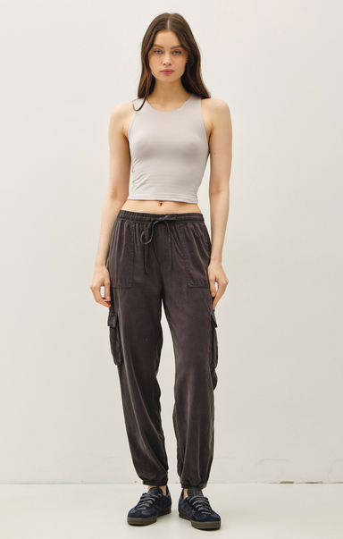 Woman wearing a beige tank top and dark cargo pants on a white background
