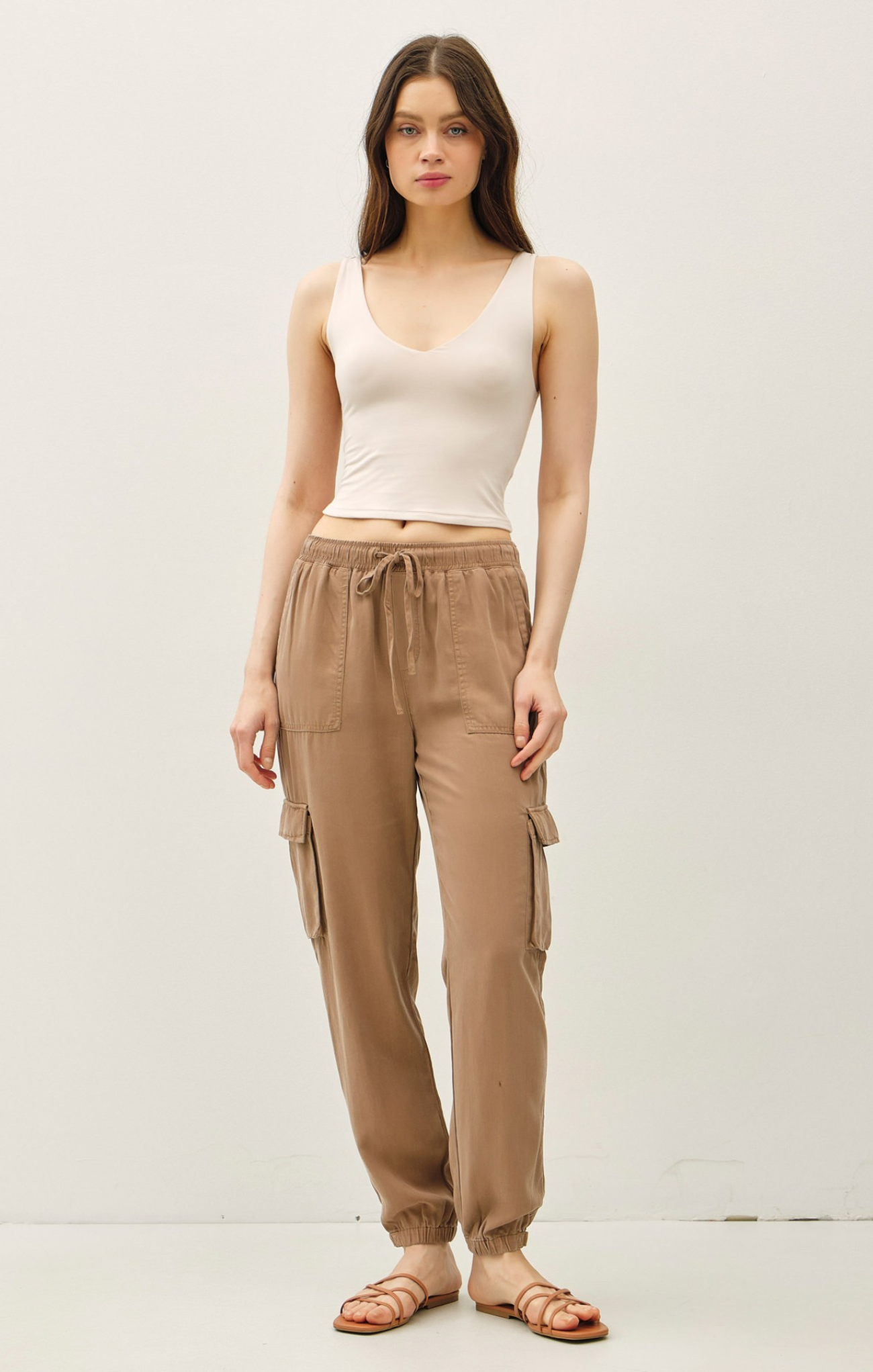 Woman wearing a white tank top and beige cargo pants on a plain background