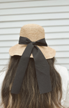 Beige straw hat with a black ribbon on a neutral background