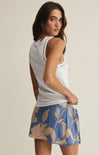 Woman wearing a white sleeveless top and blue floral skirt on a beige background